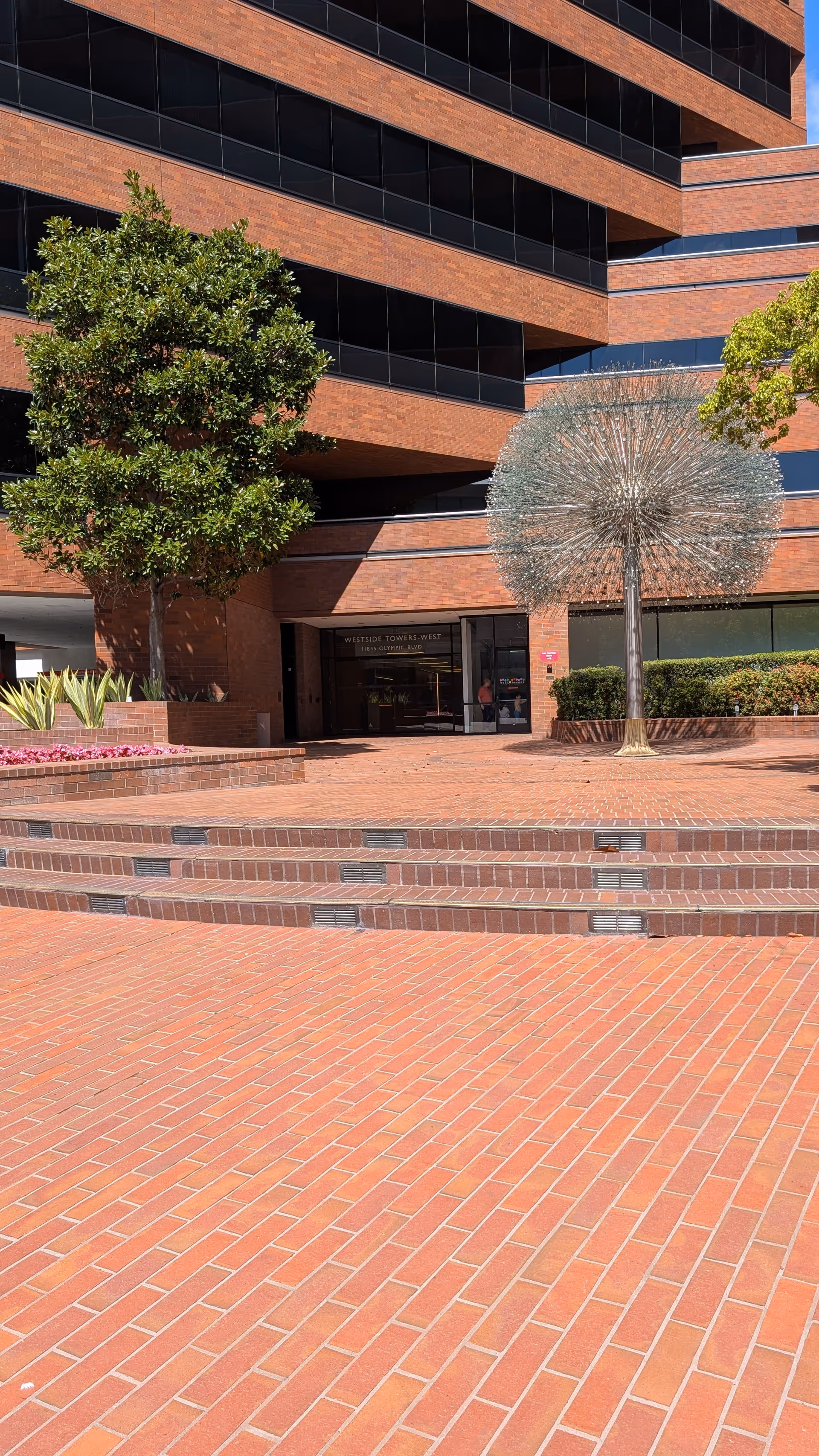 Brick exterior of a modern building with steps, trees, and a spherical sculpture.