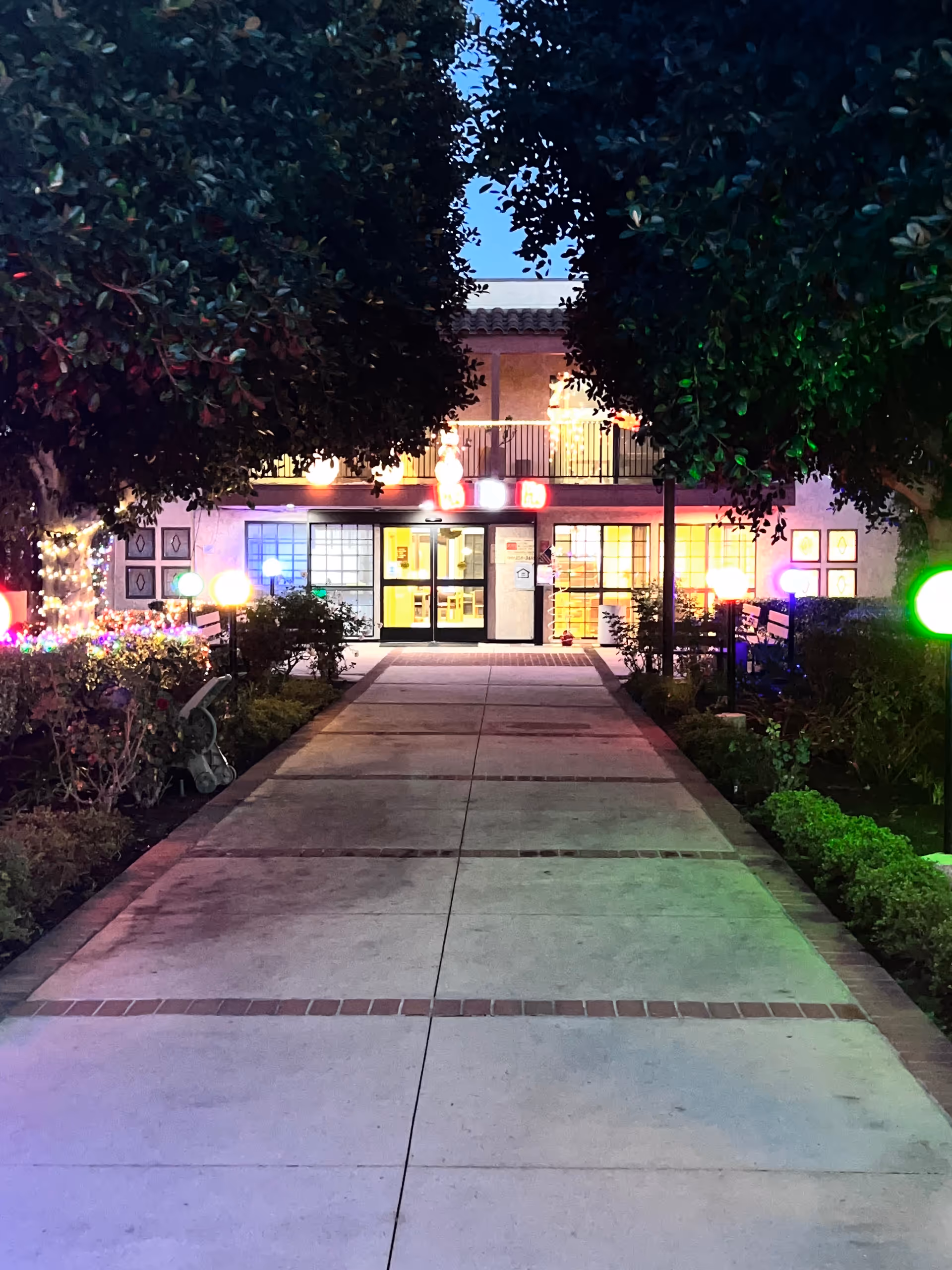 Nighttime exterior view of Canyon Terrace Senior Living with illuminated walkway and colorful lights.