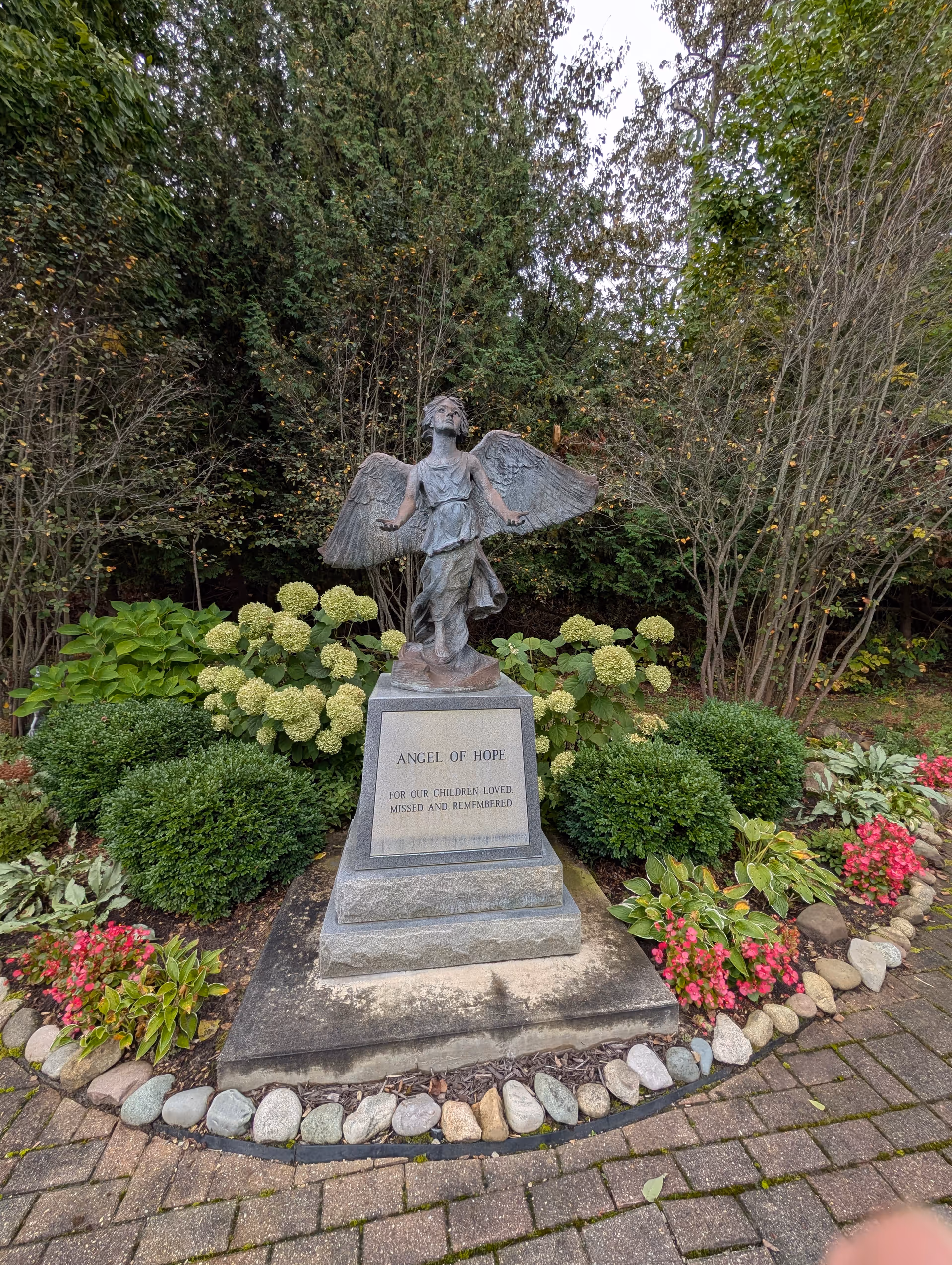 Angel of Hope statue amid a landscaped garden with shrubs and flowers.