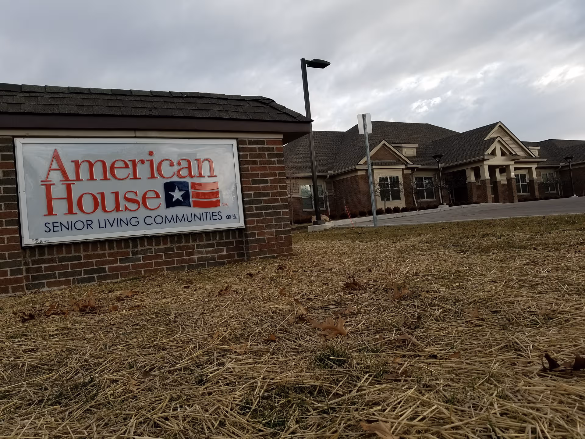 Exterior view of American House Senior Living in Rochester with brick sign and entrance.