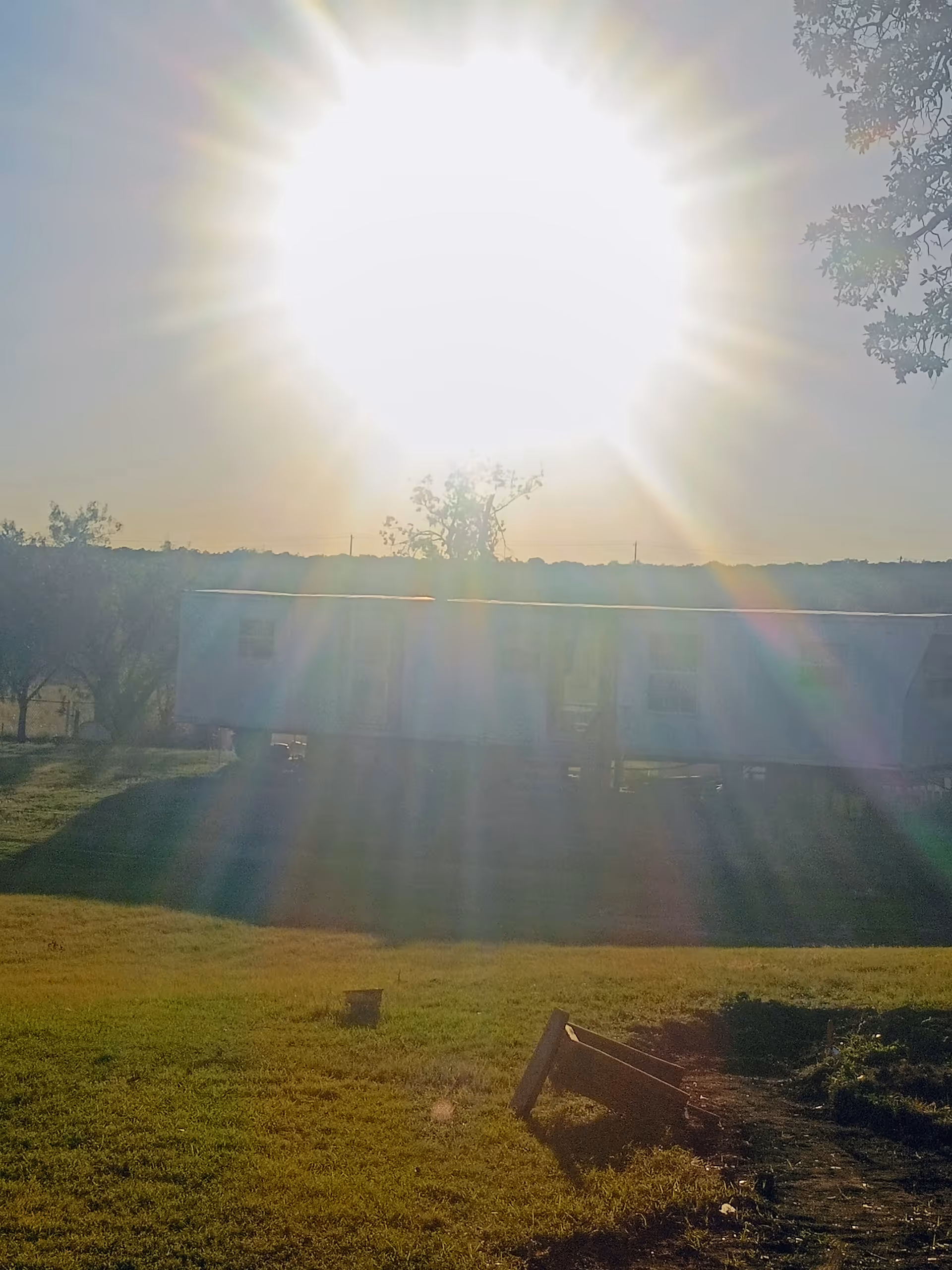Overexposed sun flare over a mobile home on a grassy lot with debris.