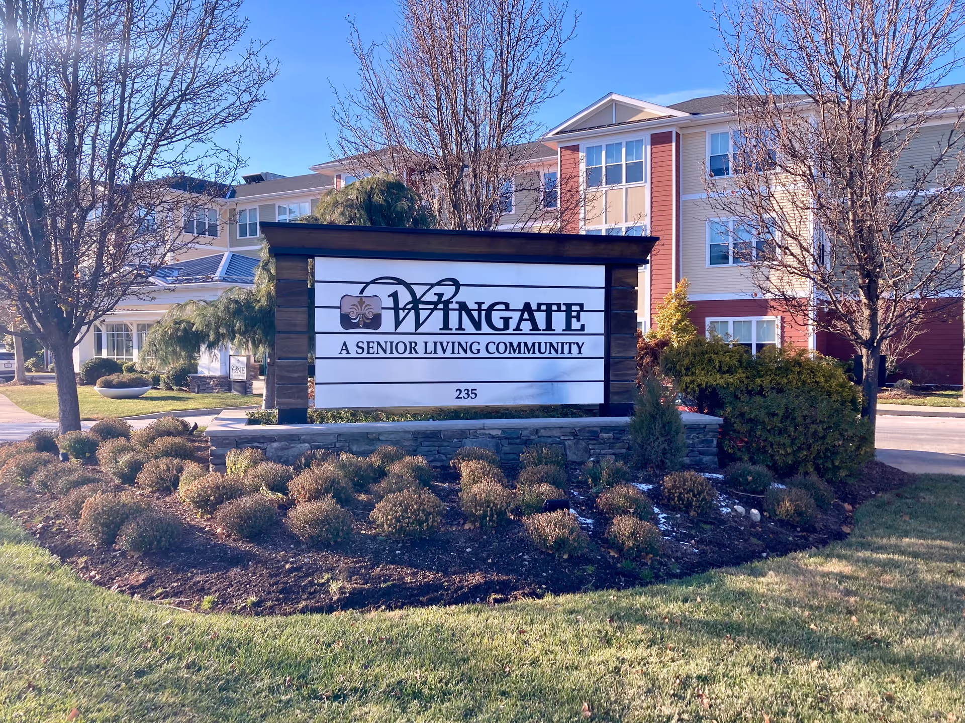 Sign for Wingate Residences at Needham, a senior living community, surrounded by landscaped gardens.