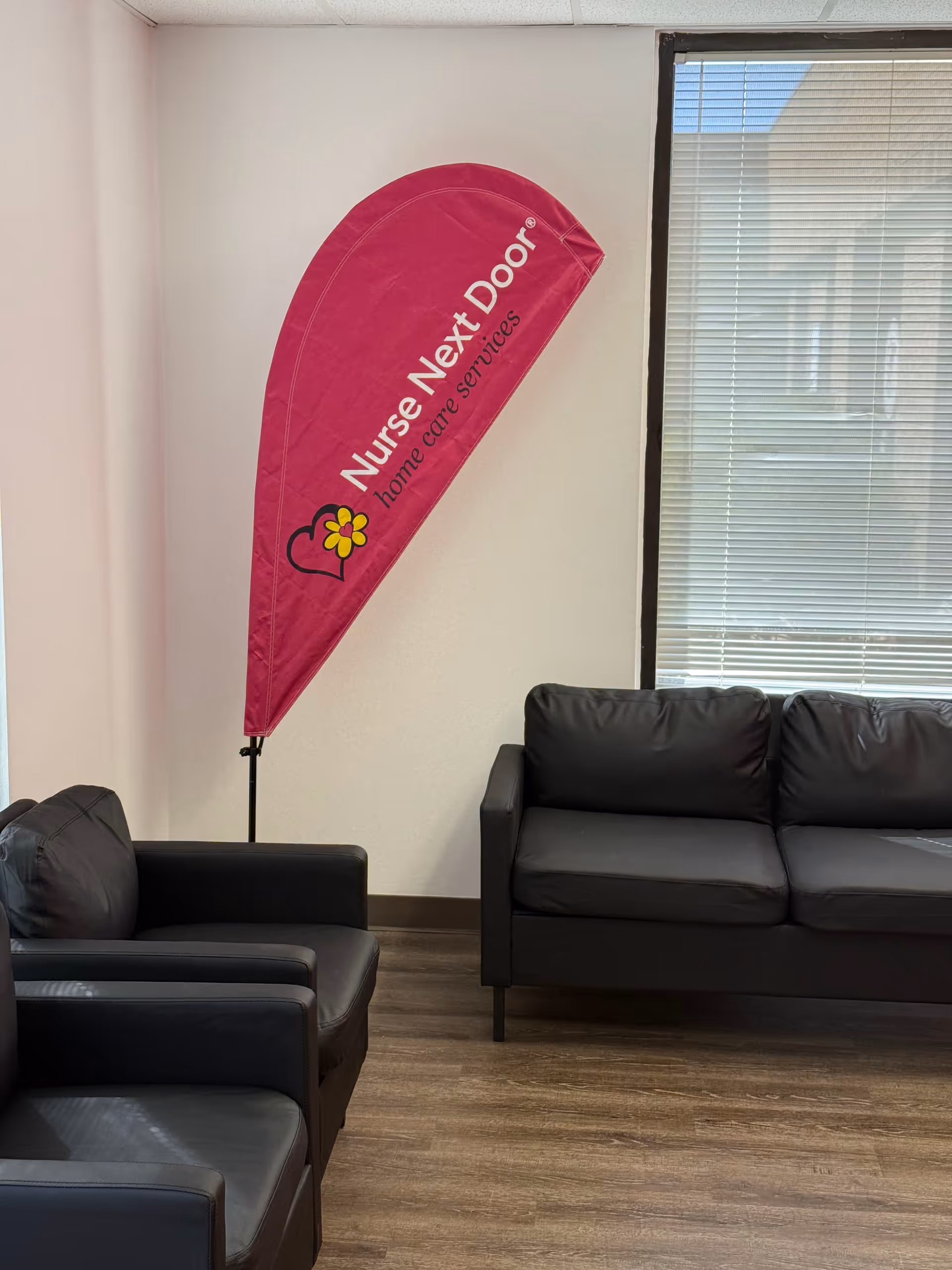 Pink Nurse Next Door banner stands beside black leather chairs in a waiting lounge.