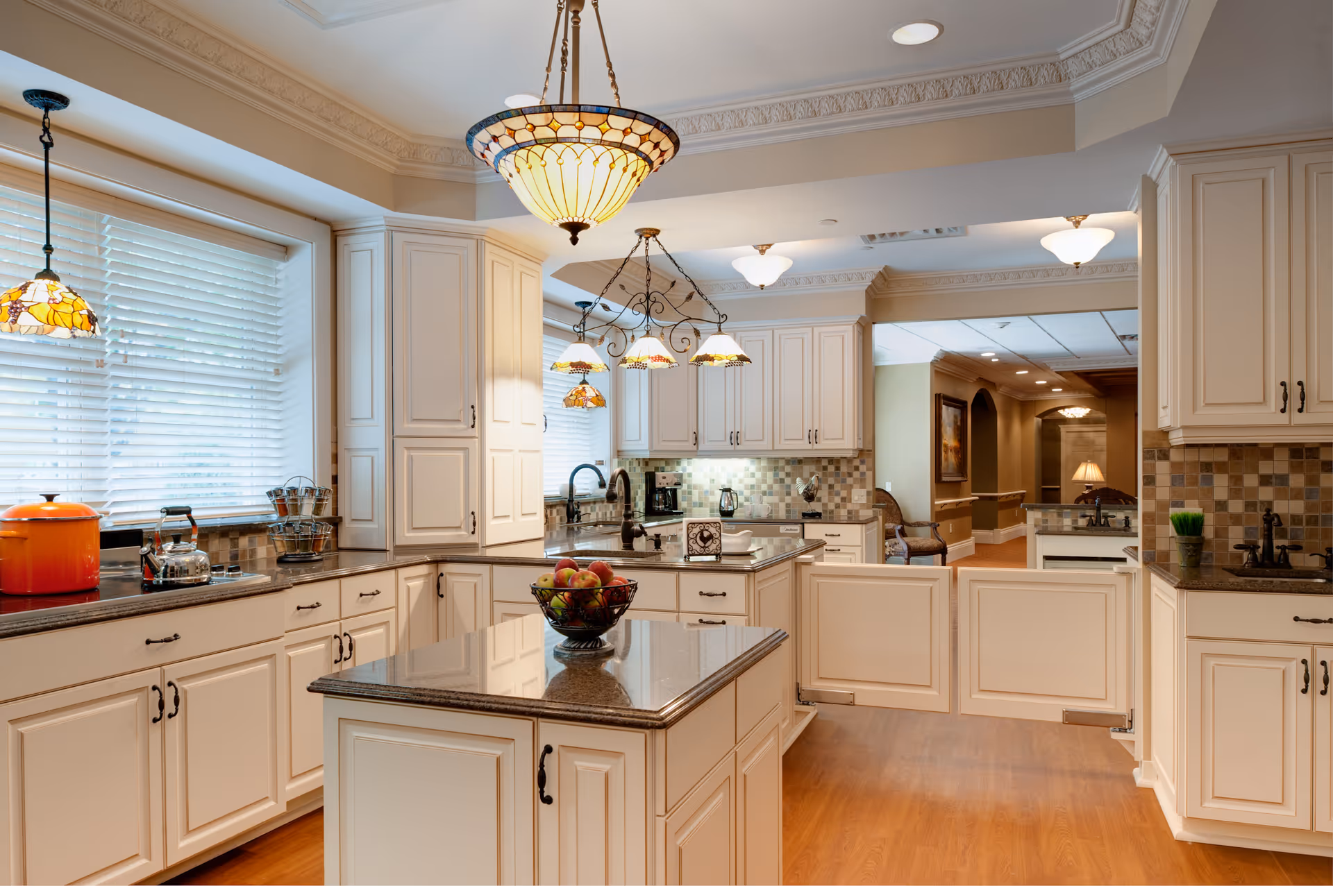 Bright white kitchen with island, pendant lights, and tiled backsplash in a senior living facility.