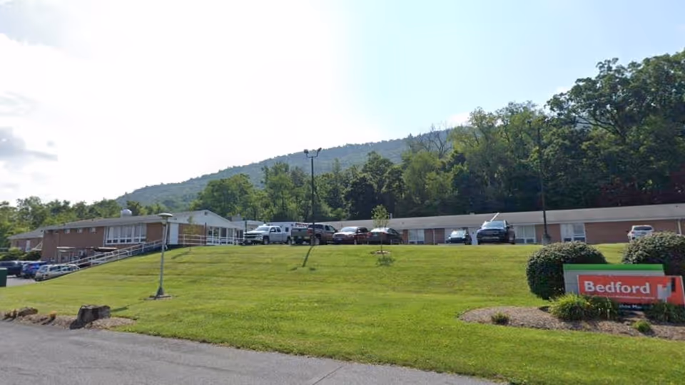 Exterior view of a single-story senior living facility with a grassy lawn and parked cars