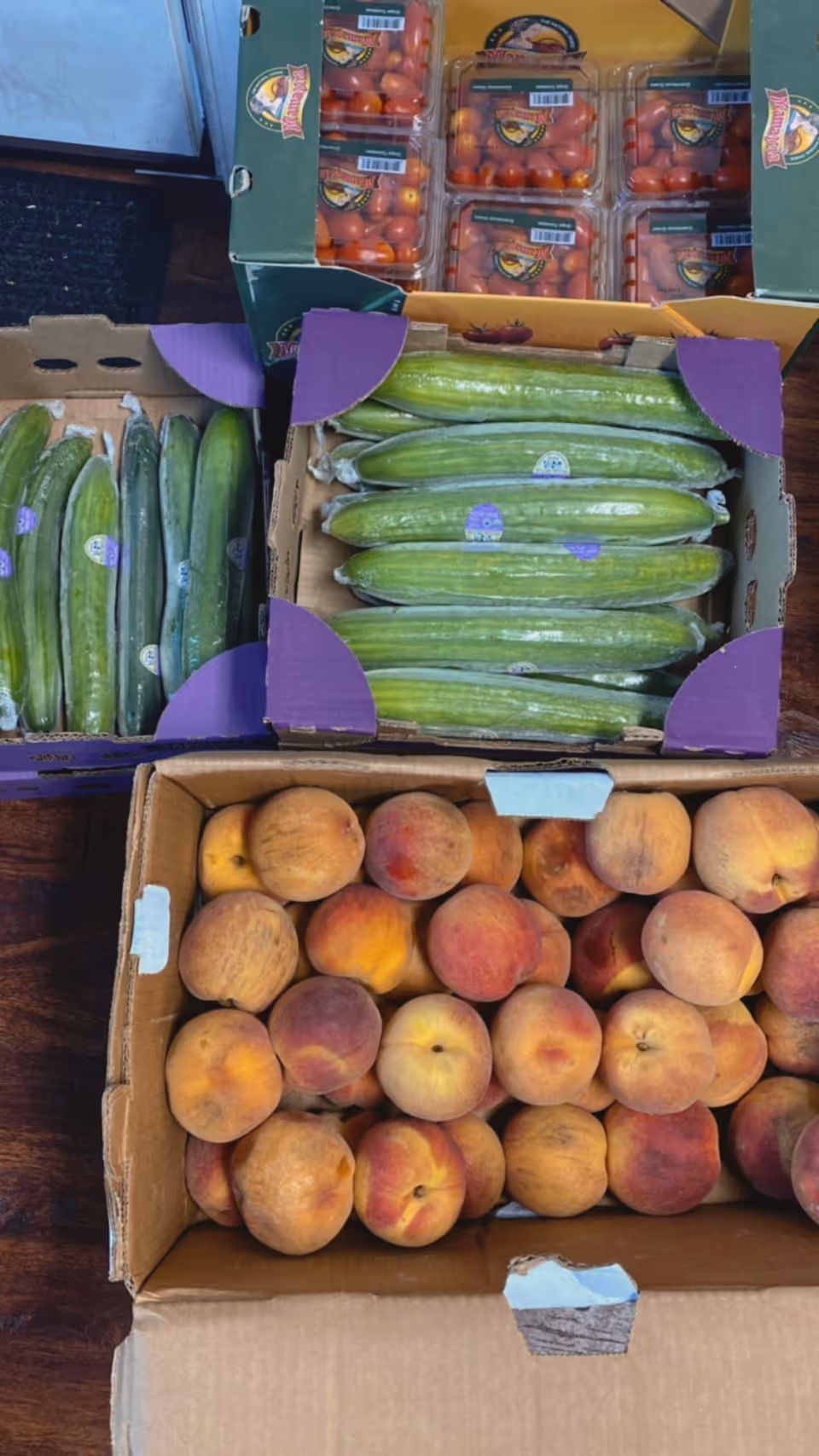 Boxes of cucumbers, peaches, and cherry tomatoes arranged in crates inside a facility.