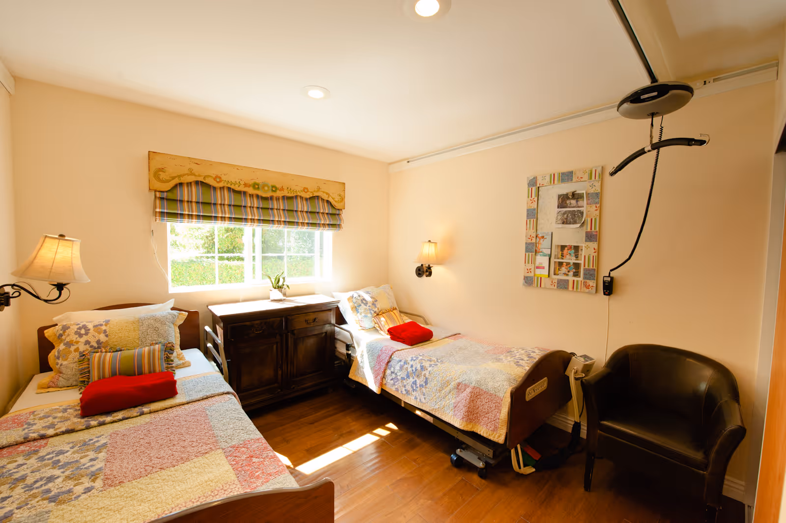Two single beds with patchwork quilts in a bright nursing home bedroom.