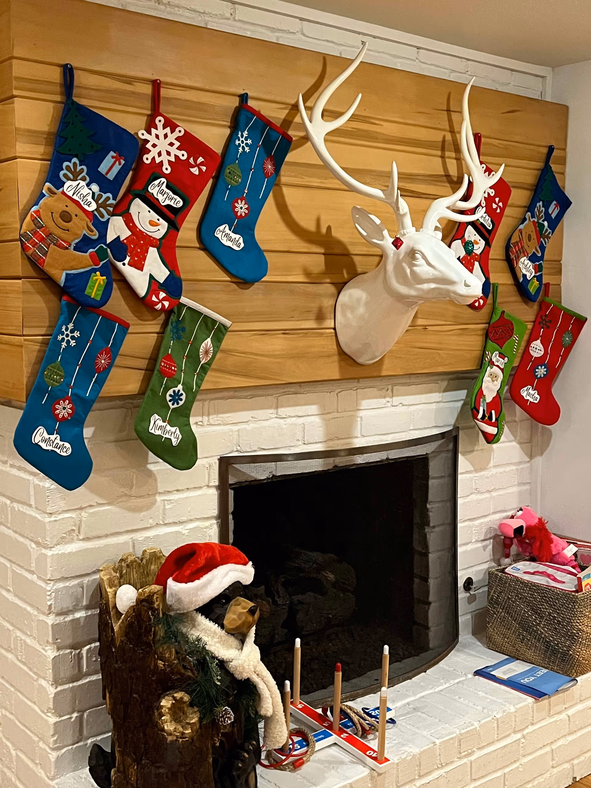 Fireplace mantel decorated for Christmas with hanging stockings, a white decorative deer head, and other holiday items.