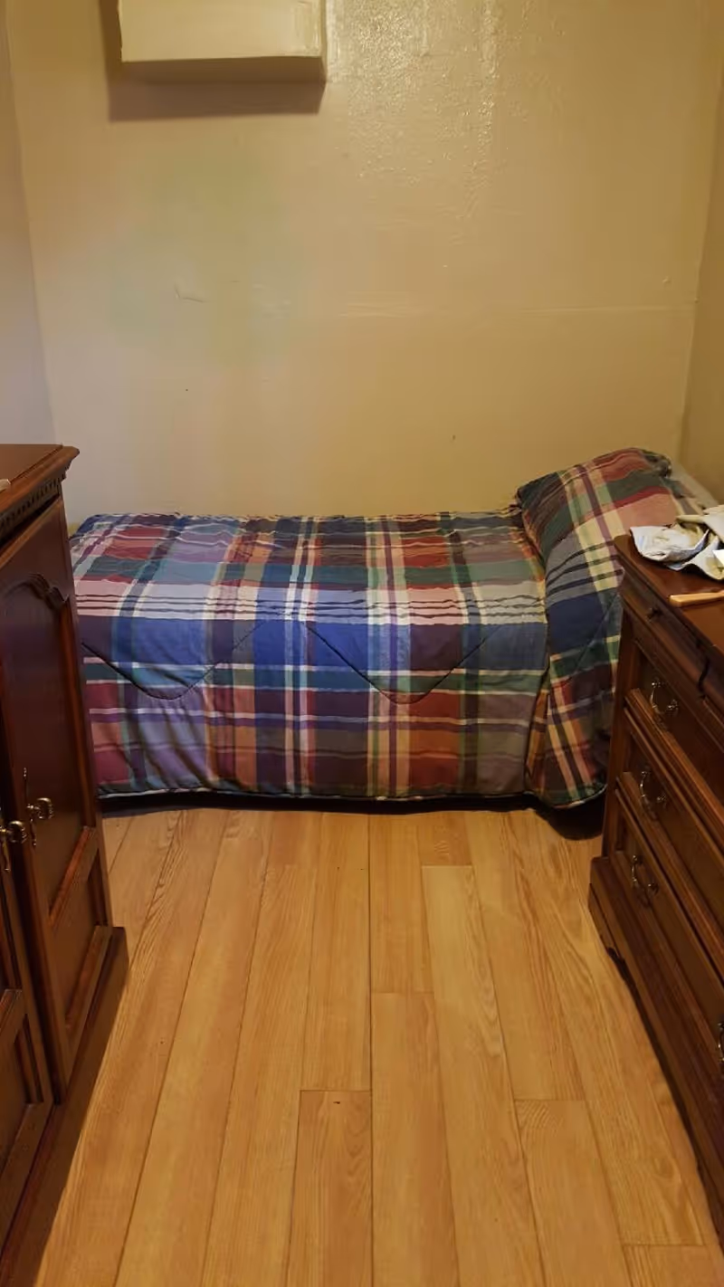 A small bedroom with a single bed covered in a plaid quilt and wooden dressers.