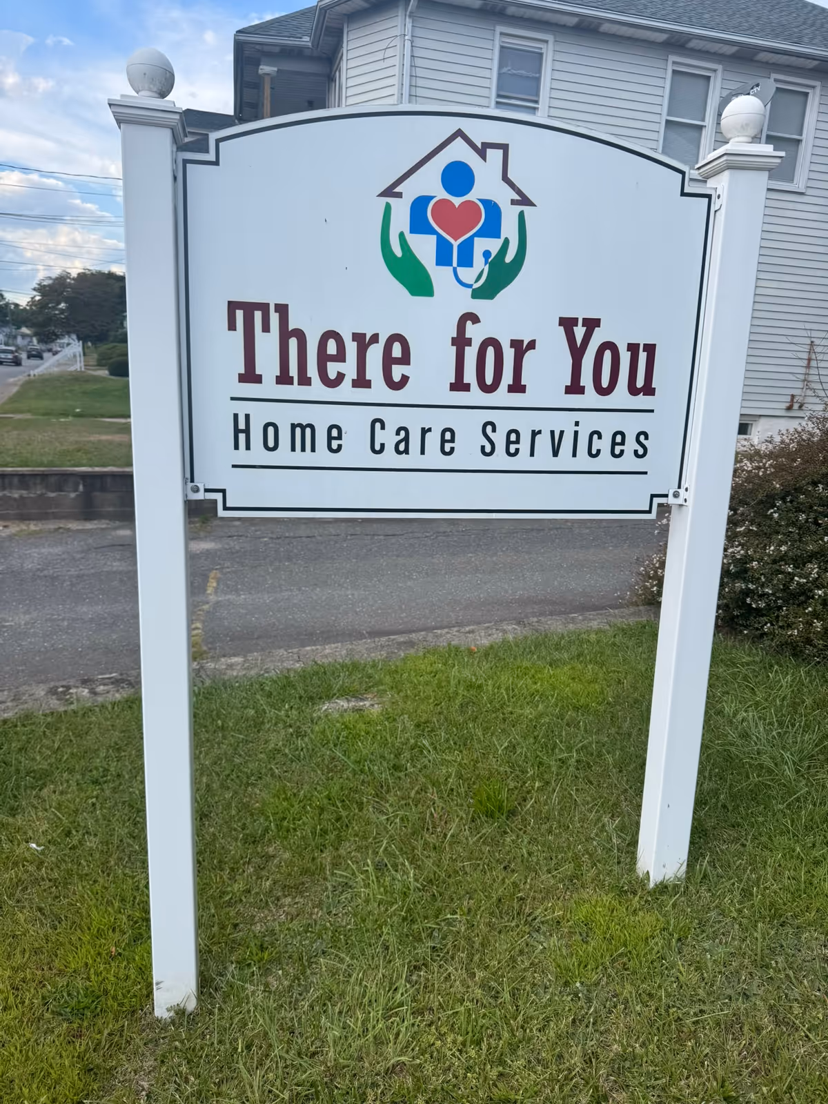 White sign with There for You Home Care Services logo stands in front of a building.