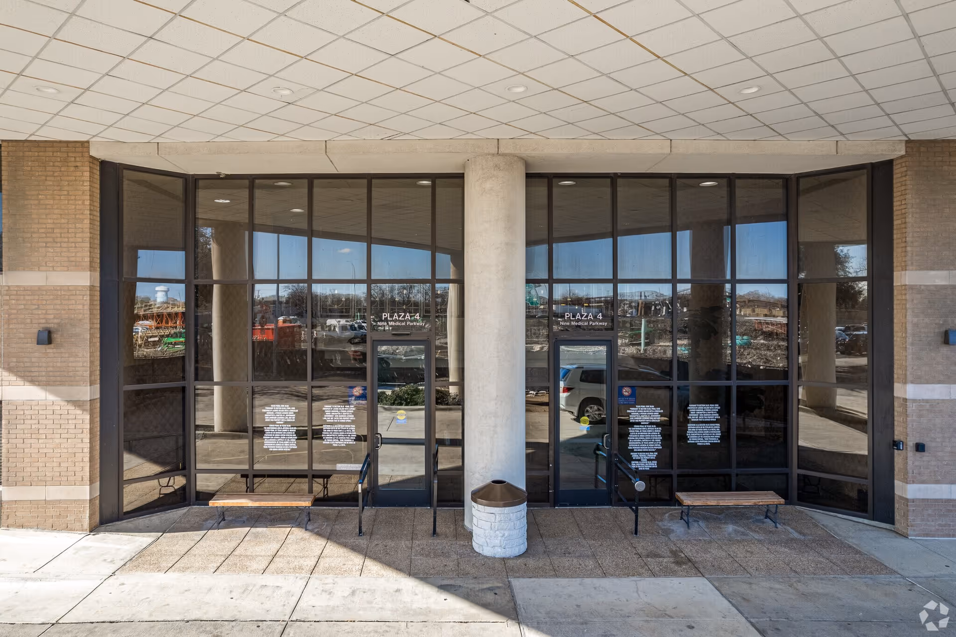 Exterior entrance of a brick building with large glass doors and benches outside.
