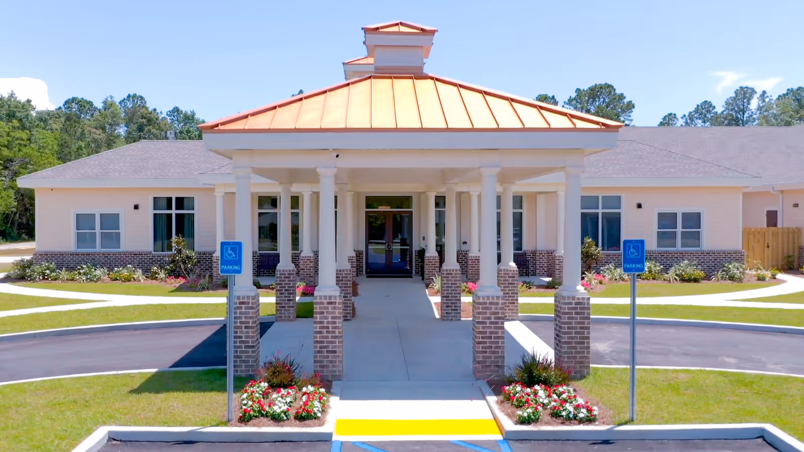 Front entrance of a light-colored assisted living building with columns and handicap parking.