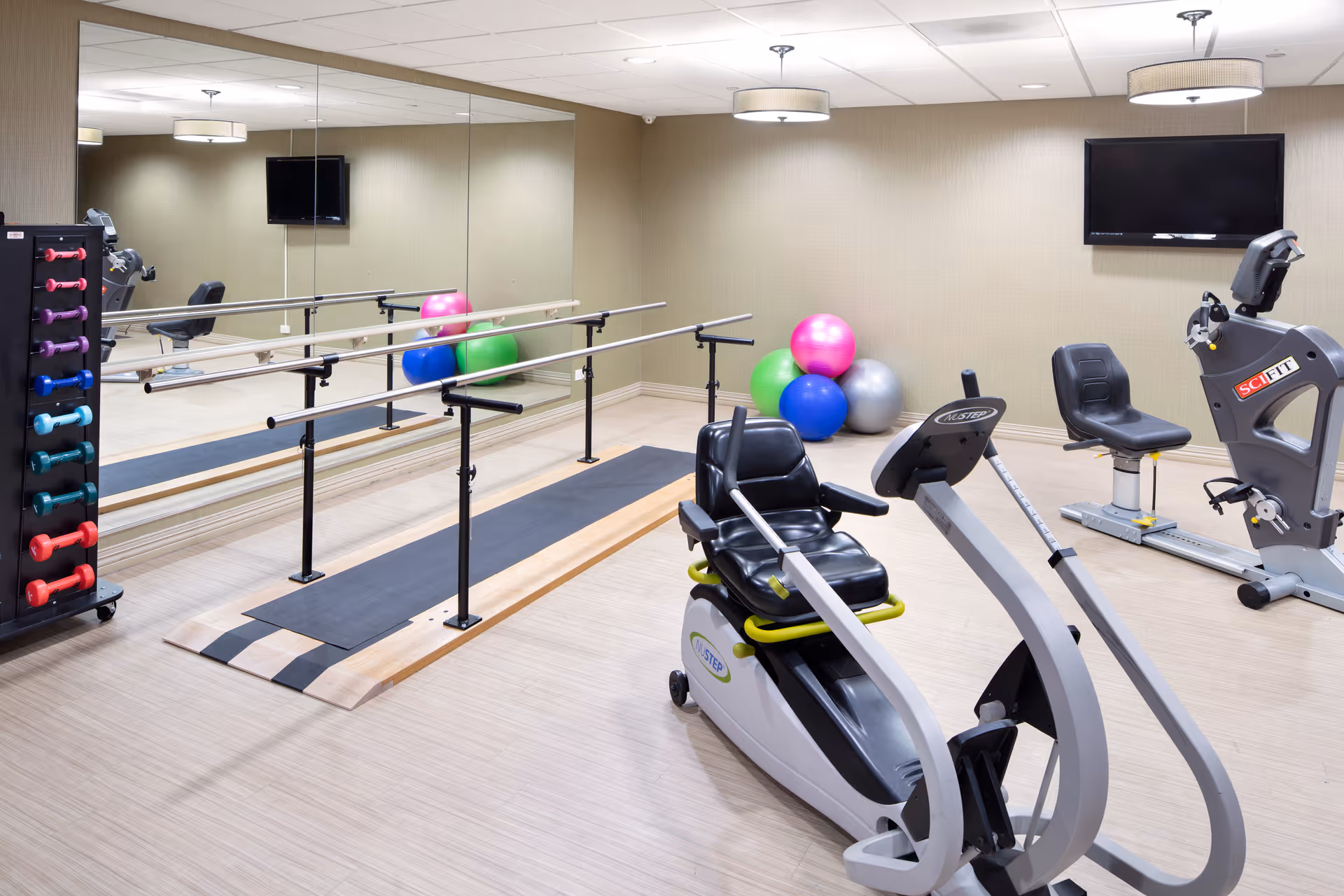 Bright senior fitness room with mirrors, treadmills, stationary bike, weights, and exercise balls.