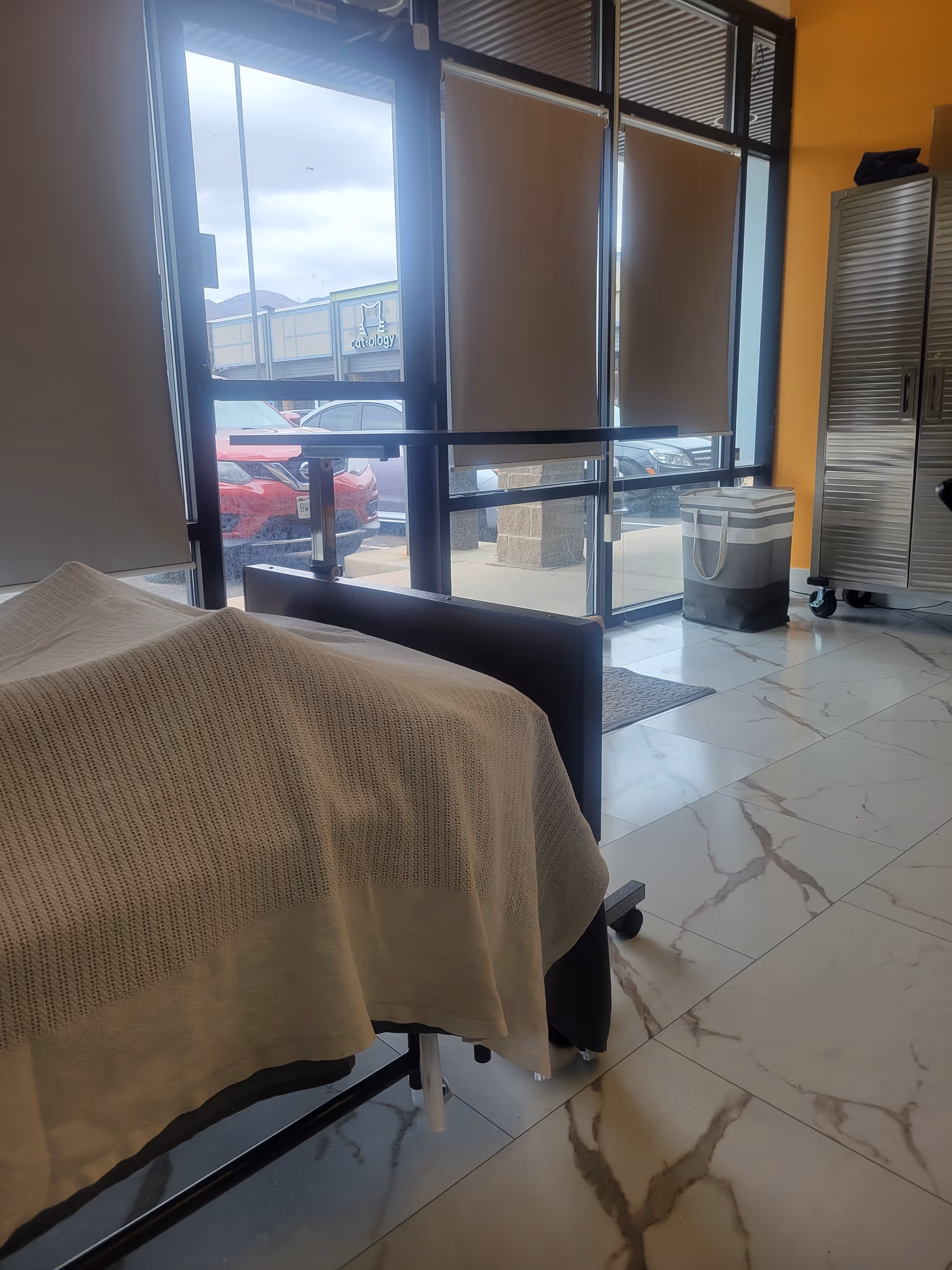 Hospital-style bed in a well-lit patient room with blinds, cabinets, and marble floors.