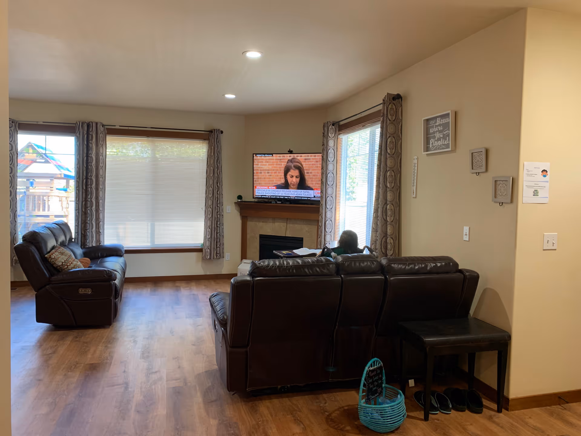 Cozy living room with brown leather sofas, a fireplace mantle, TV, and large windows with curtains.
