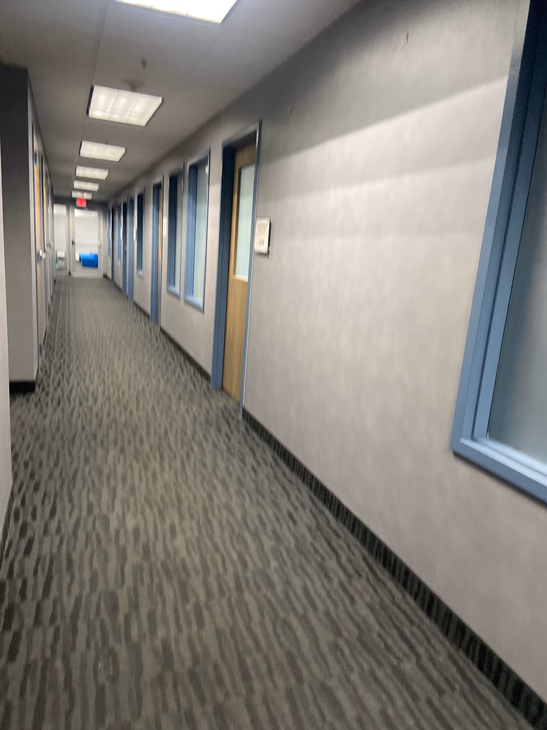 Long indoor hallway in a senior living facility with multiple doors and windows.