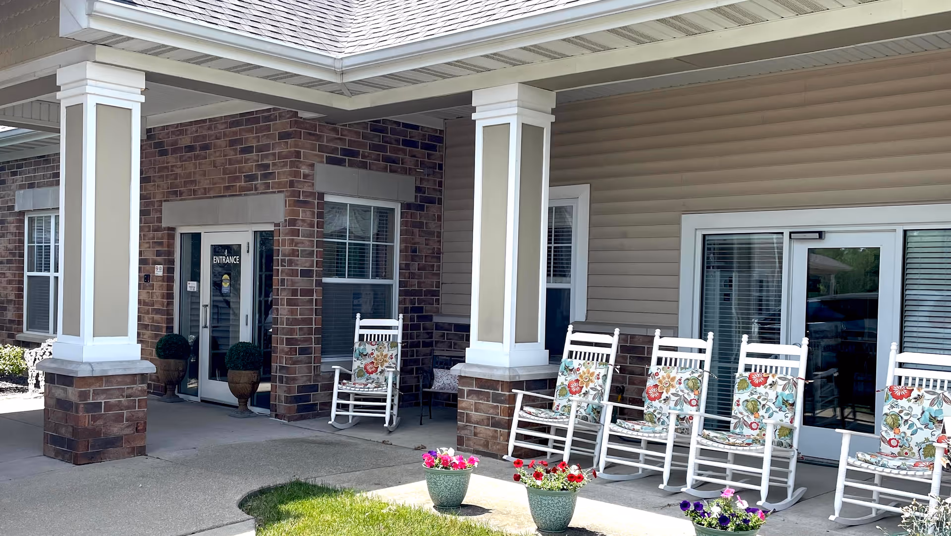 Covered front entrance with brick columns and several white rocking chairs with floral cushions on the porch.
