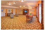 Spacious senior living lounge with patterned carpet, seating, and dining tables.