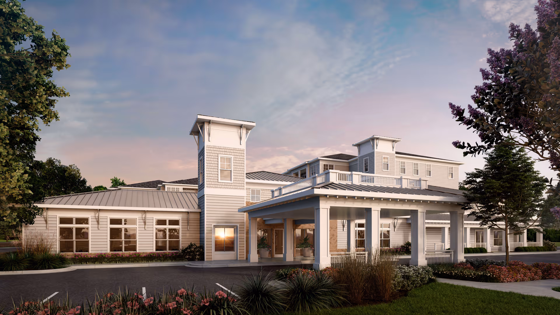 Exterior view of a senior living facility building named Overture West Ashley during sunset, featuring a covered entrance, multiple windows, and landscaped greenery with trees and flowers.