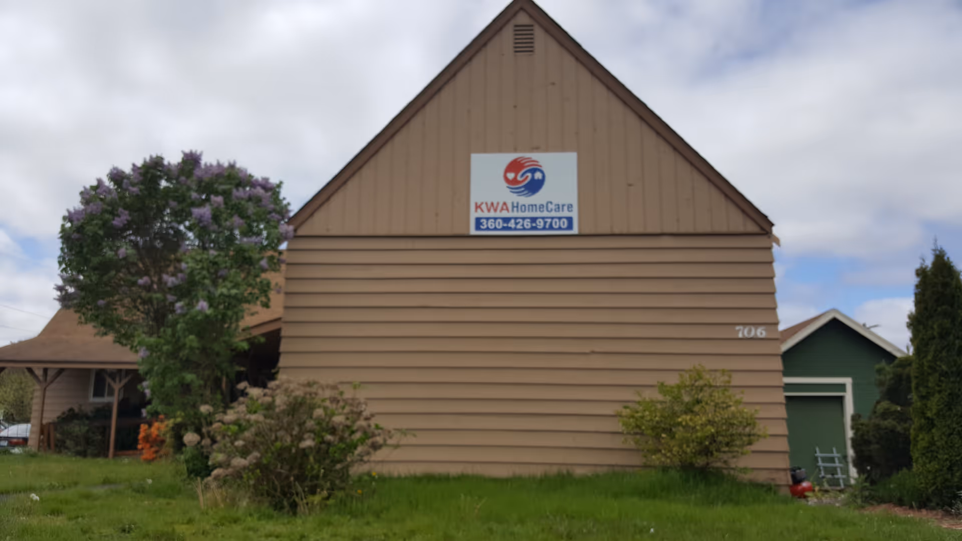 Brown building with a KWA HomeCare sign, surrounded by shrubs and trees in a grassy lot.