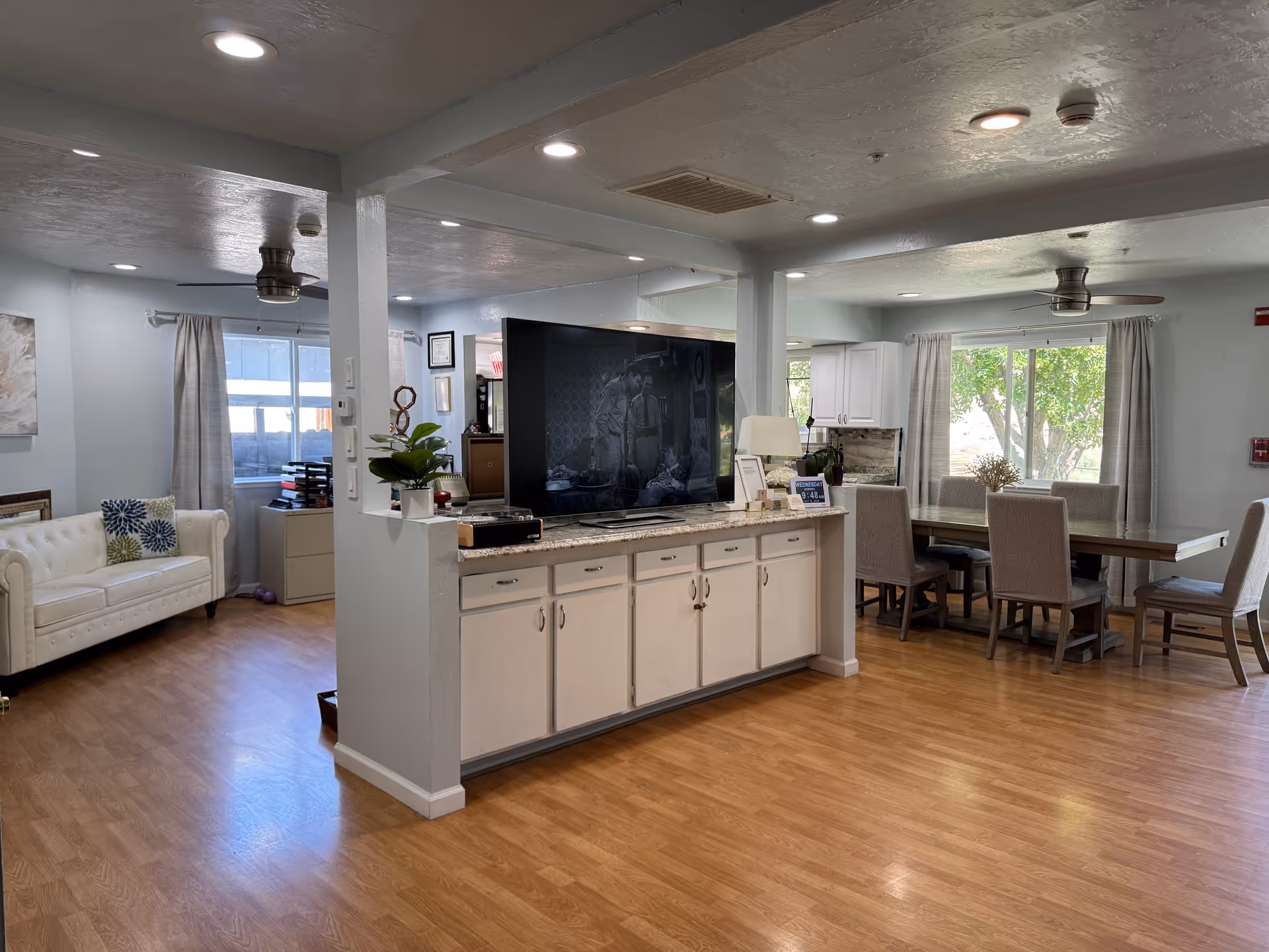 Open communal area with TV, white sofa, and a dining table.