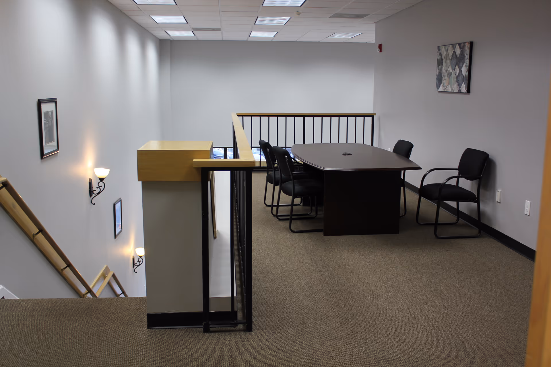 Interior seating area with a rectangular table and several chairs near a stair railing.