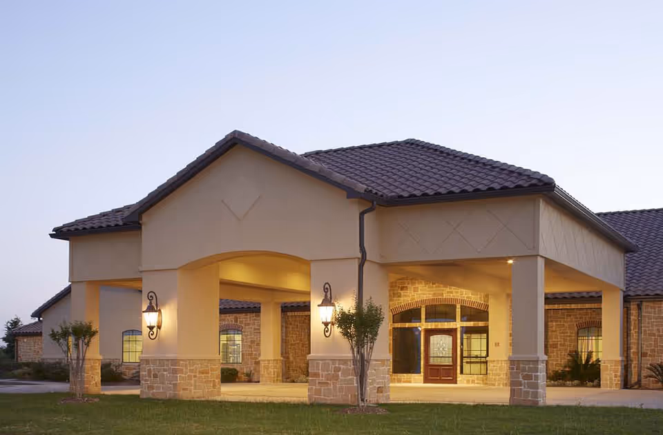 Front view of a beige senior living facility entrance with stone columns and lanterns.