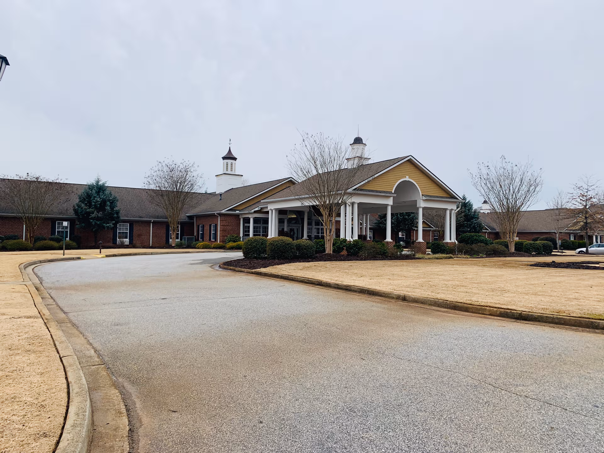 A curved driveway circles toward a brick senior living facility with a covered front entrance.
