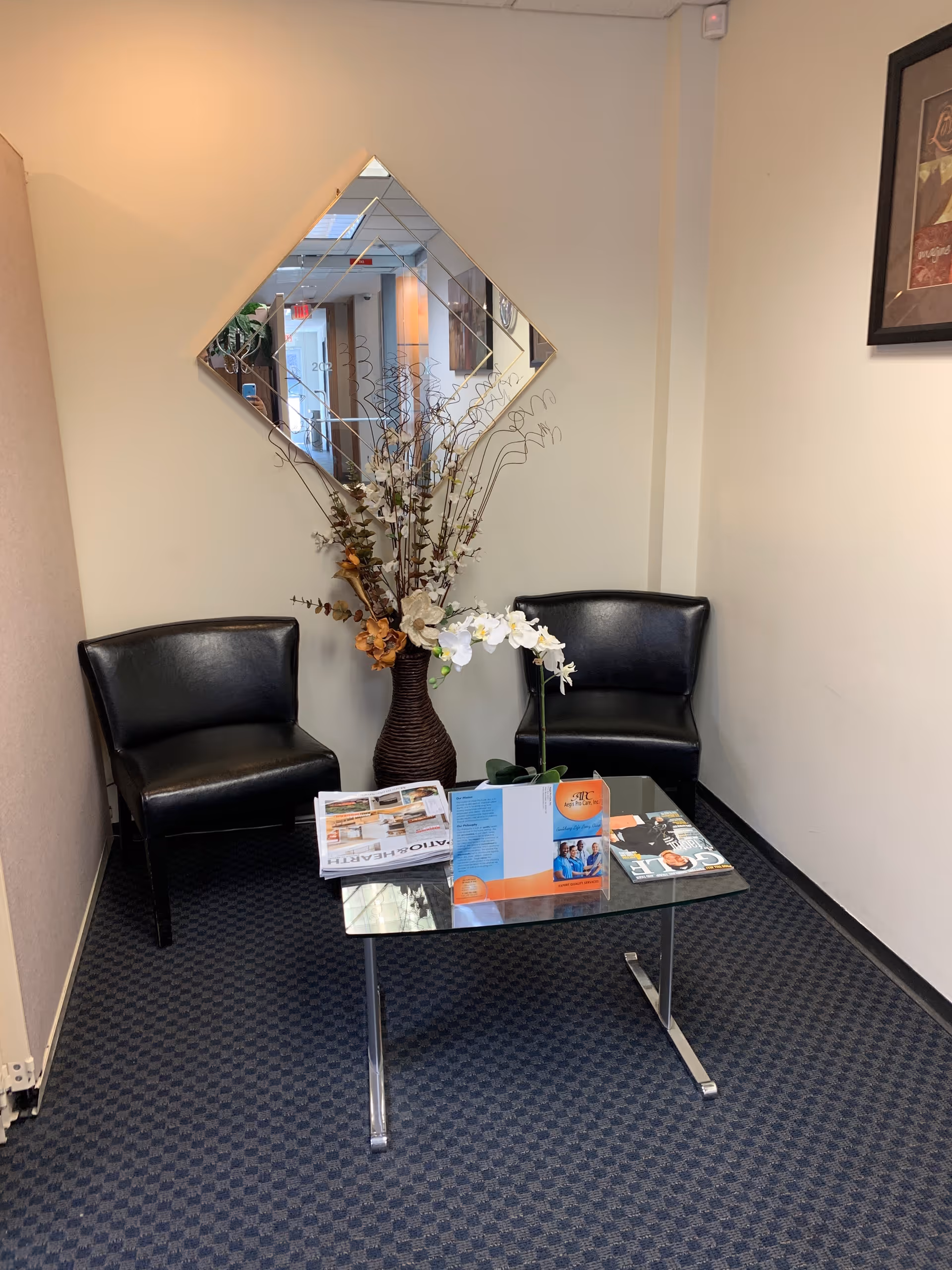 Two black leather chairs flank a glass coffee table in a small waiting area.