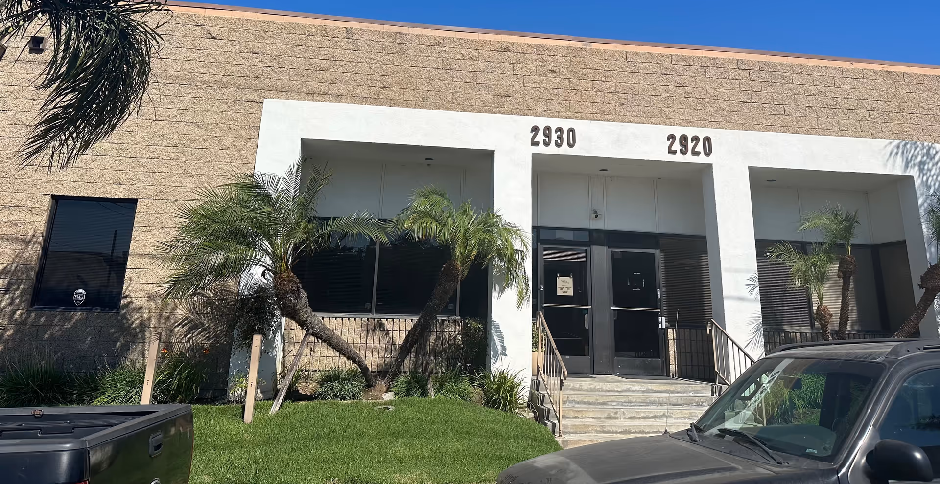 Front entrance of a beige building with numbers 2930 and 2920, and palm trees.