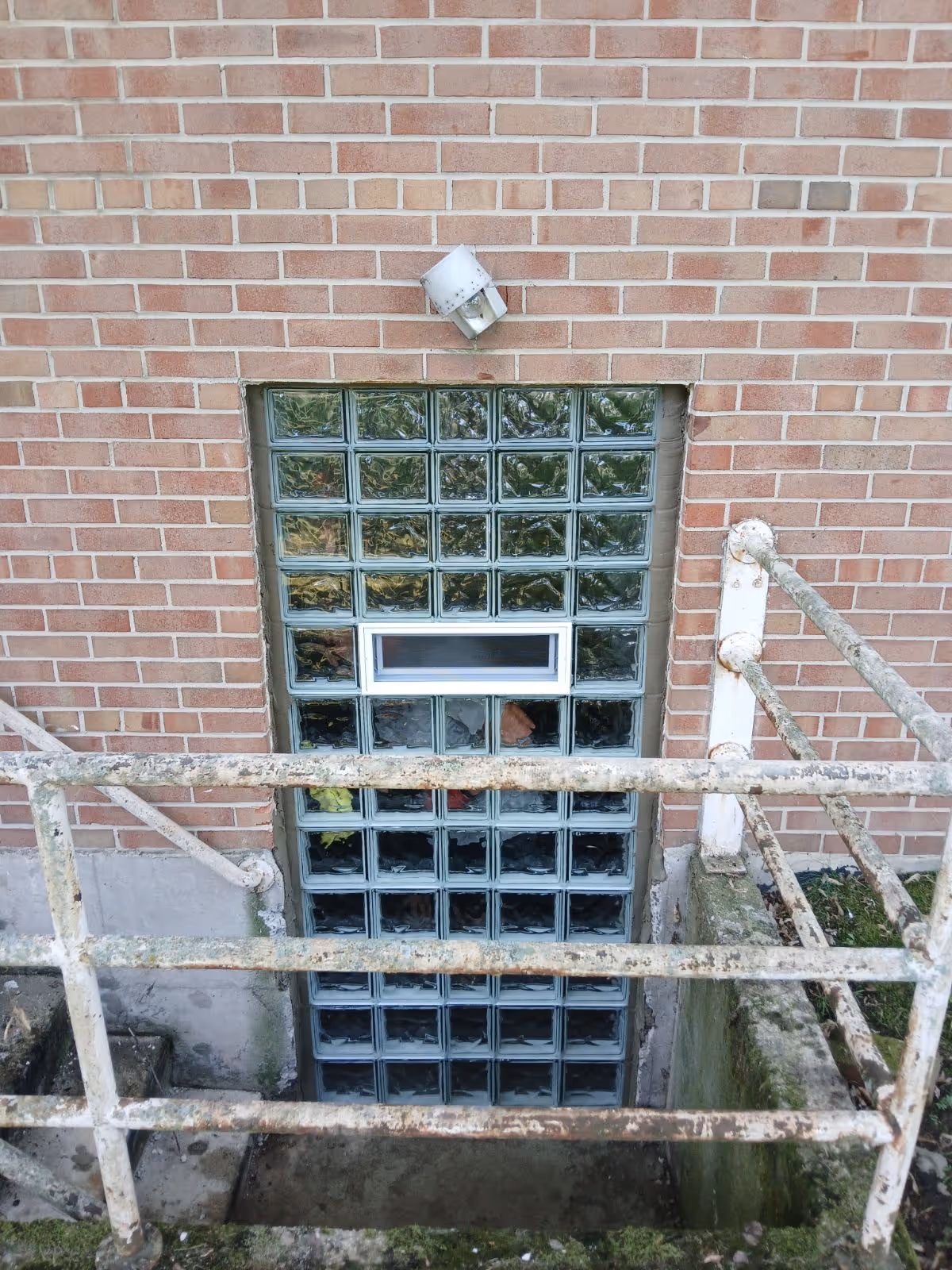 Rusty railing frames a glass-block exterior door leading to a basement entry.