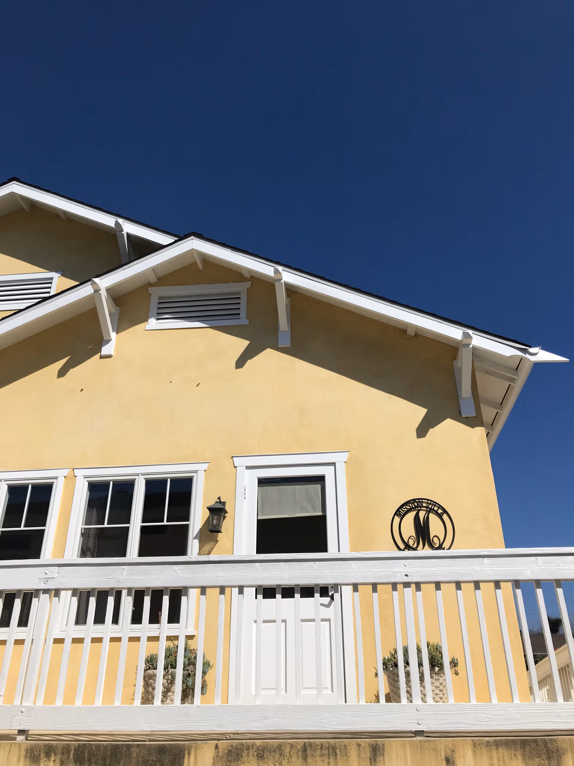 Yellow building with white trim, balcony railing, and a clear blue sky.