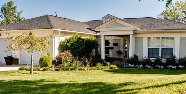 Front exterior of a single-story residential-style building with a porch, garage, and landscaped lawn.