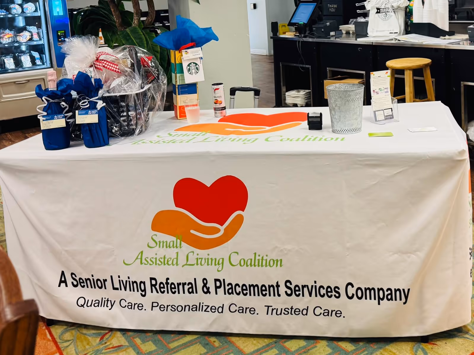 Indoor event table with banner reading 'Small Assisted Living Coalition' on white tablecloth.
