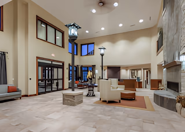 Spacious high-ceilinged interior lobby with seating areas, indoor lamp posts, large windows, and a fireplace.