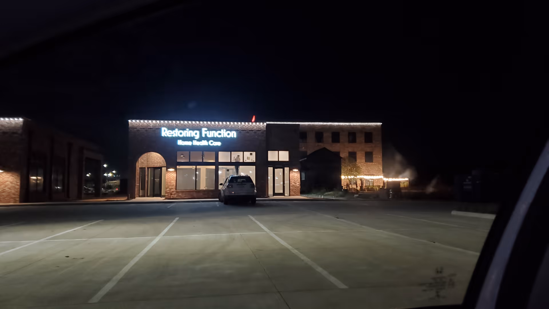 Nighttime exterior of Restoring Function Home Health Care building with illuminated sign and parked car.