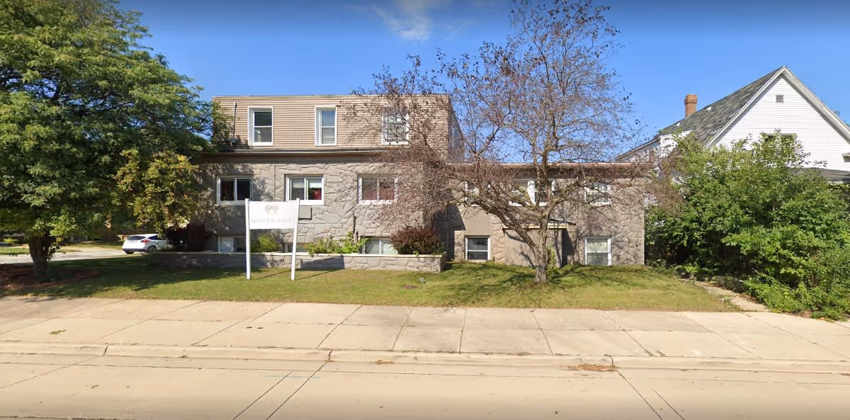 Stone-faced two-story residential building with a lawn, trees, and a front sign for Golden View.