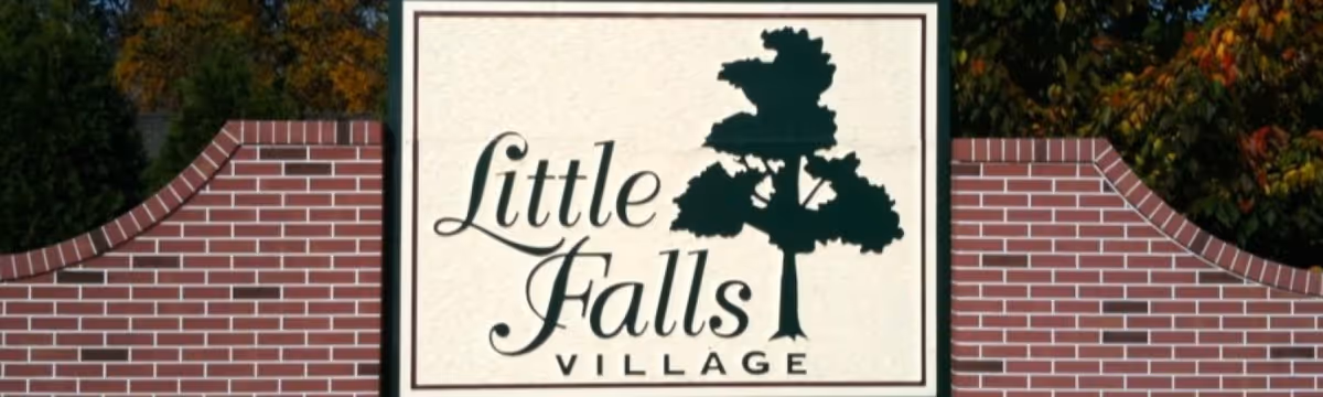 Exterior entrance sign reading 'Little Falls Village' between curved brick walls.