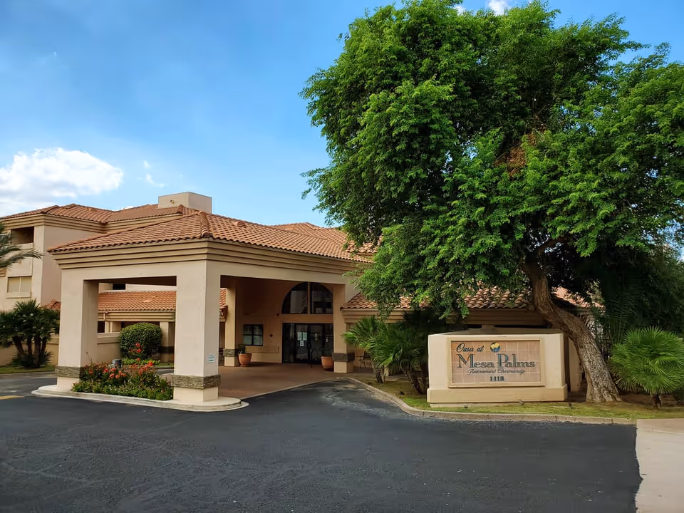 Exterior view of Oasis at Mesa Palms facility showing the entrance with a covered driveway, beige building with a tiled roof, a large tree, and a sign with the facility name and address.