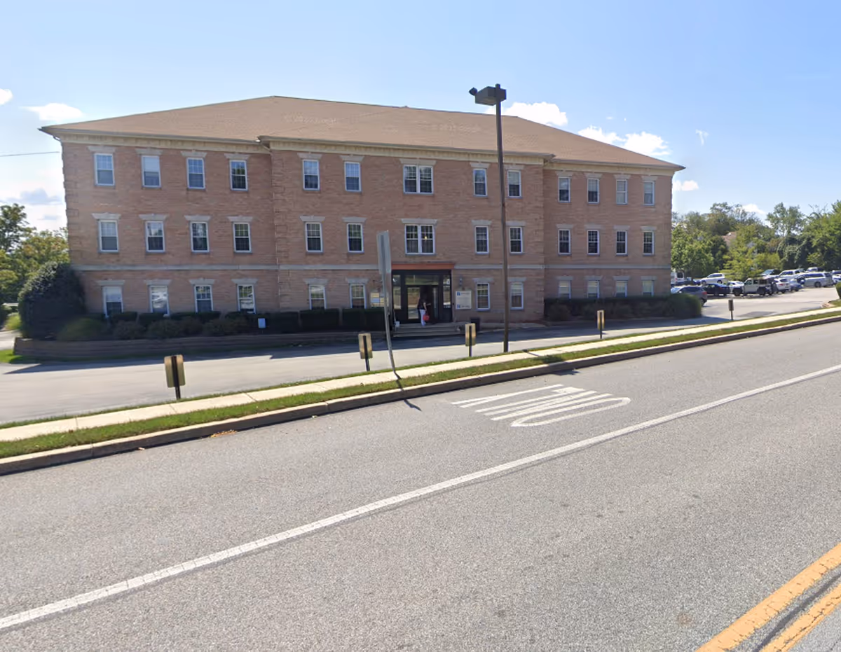 Brick senior facility building viewed from street with entrance and surrounding parking.