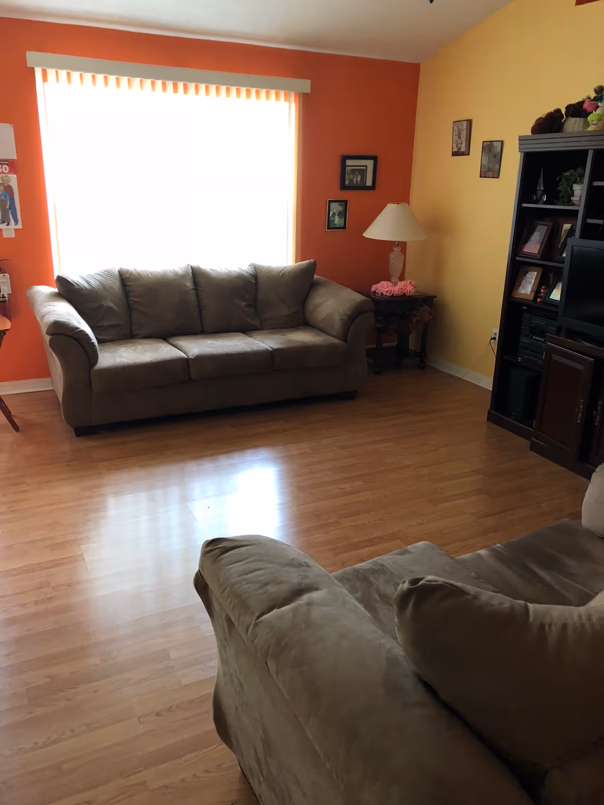 Bright living room with beige sofa, yellow and orange walls, lamp, and shelves.