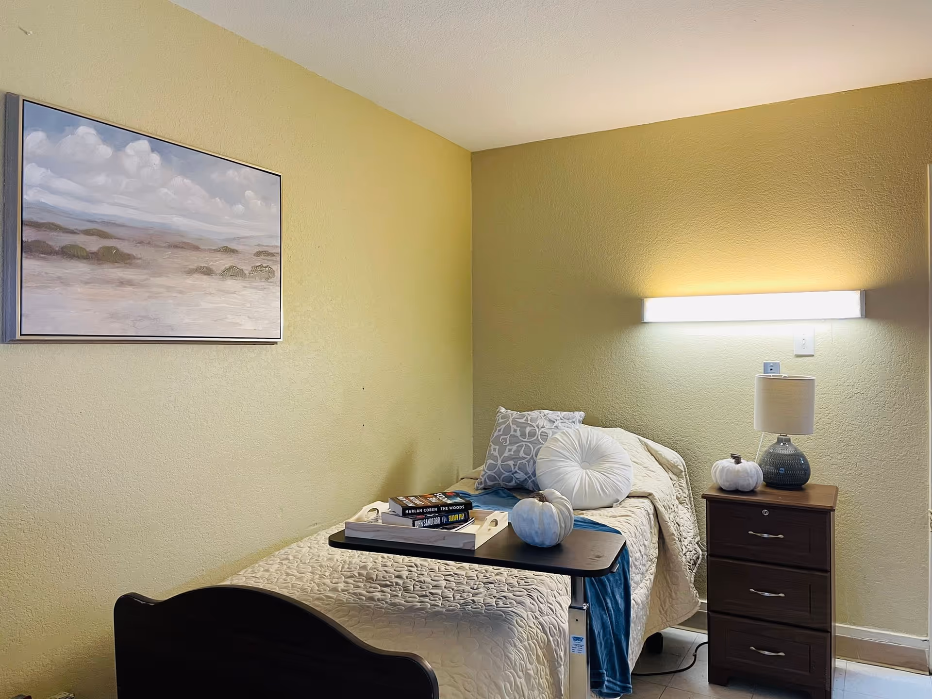 Single guest room bed with tray, lamp, and painting in yellow-painted bedroom.