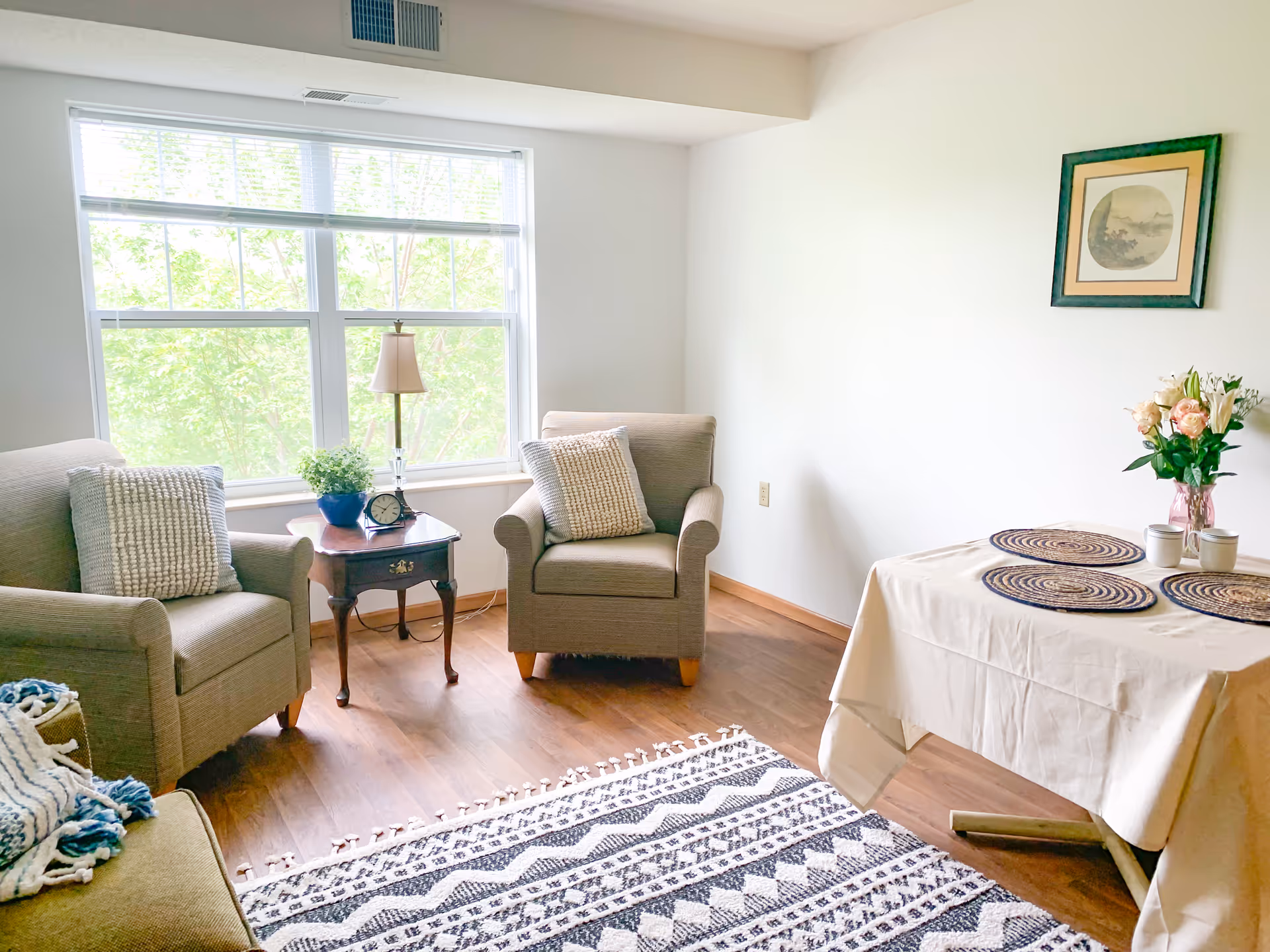 Cozy living room with two gray armchairs, a side table, large window, and dining table.