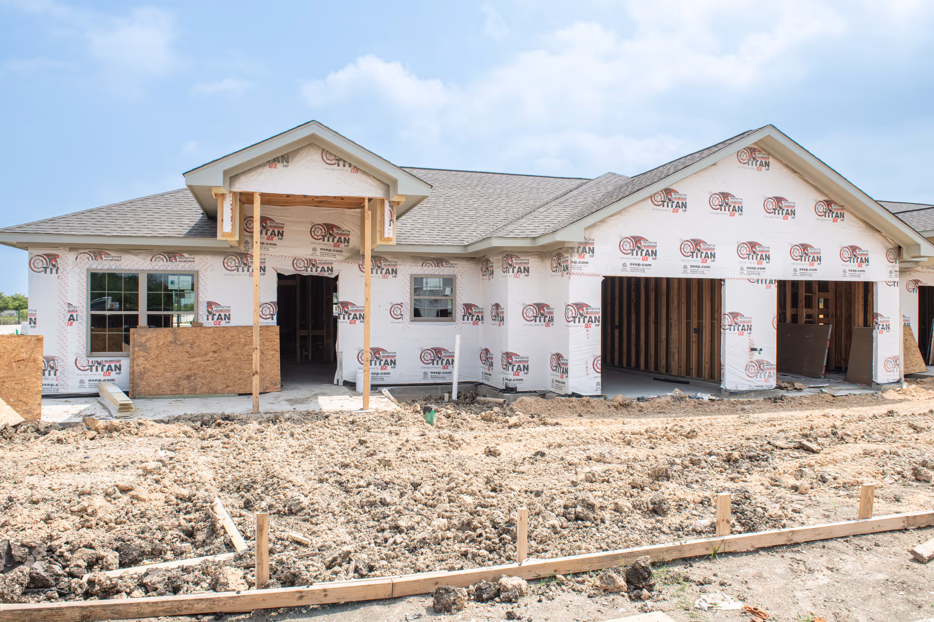 Under-construction, single-story senior living building with white weather-wrap and dirt foreground.