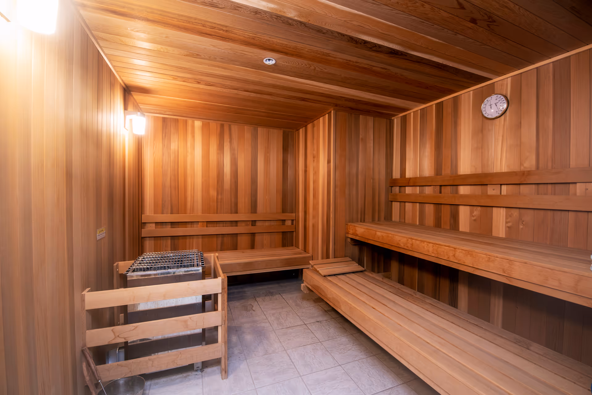 Interior of a wooden sauna with tiered benches, a heater, and a wall clock.