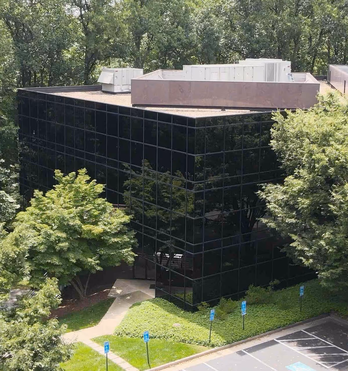 A modern, black glass office building surrounded by trees and a small entrance walkway.