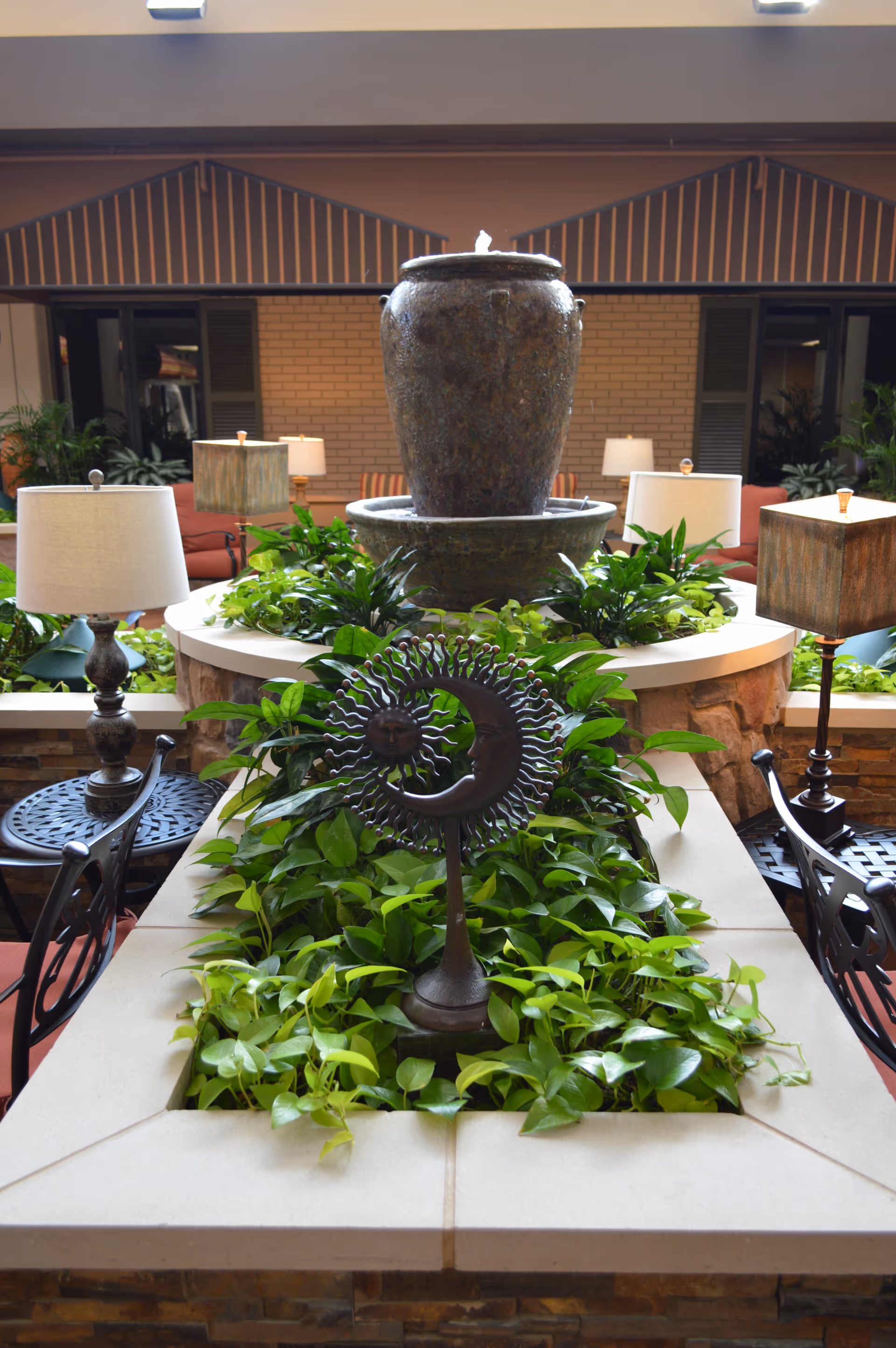 Indoor senior living lobby with a central fountain, greenery, and seating.