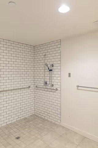 Accessible bathroom shower with white subway tiles, grab bars, and a handheld shower.