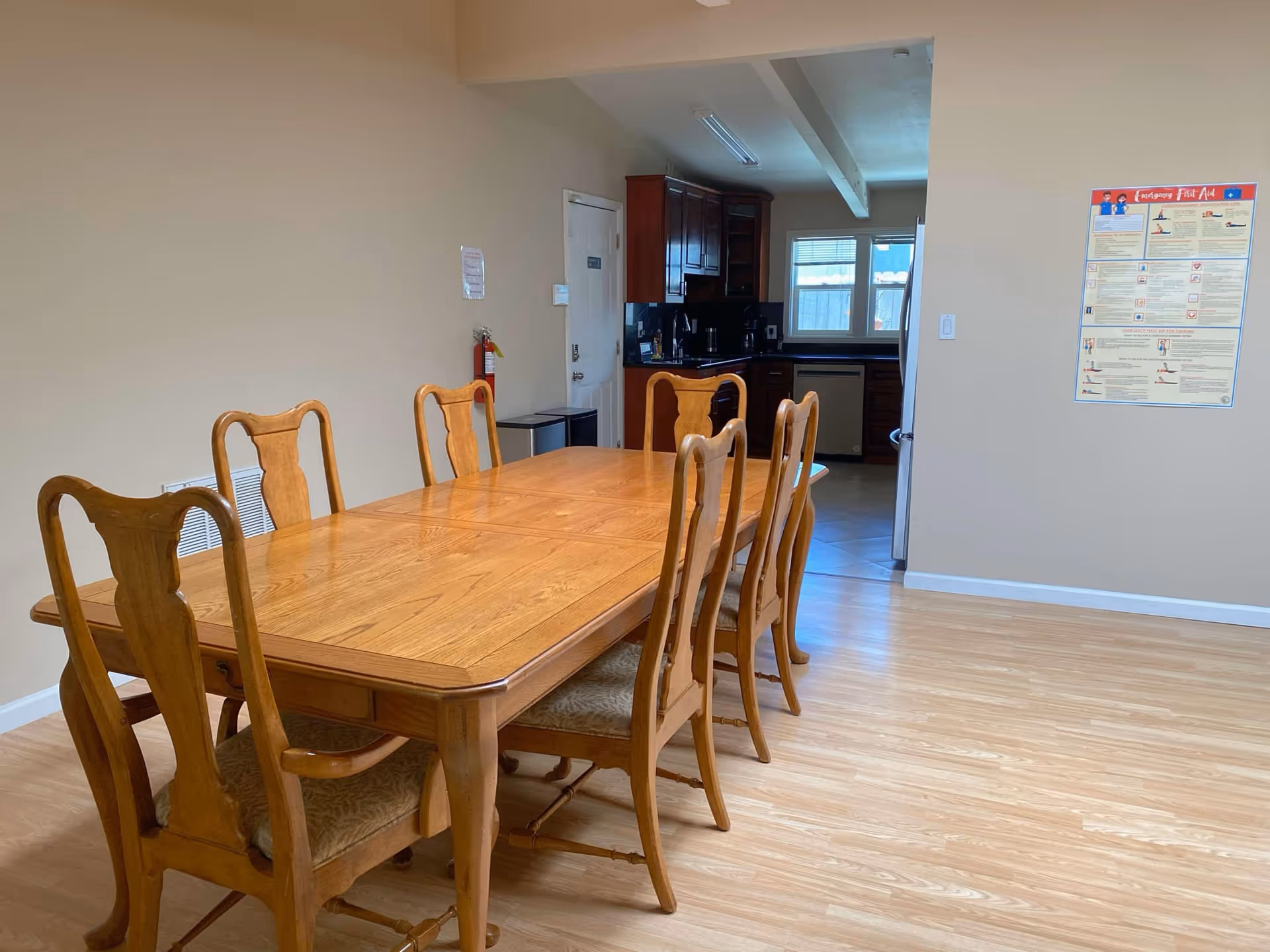Wooden dining table with multiple chairs in a spacious beige dining area.