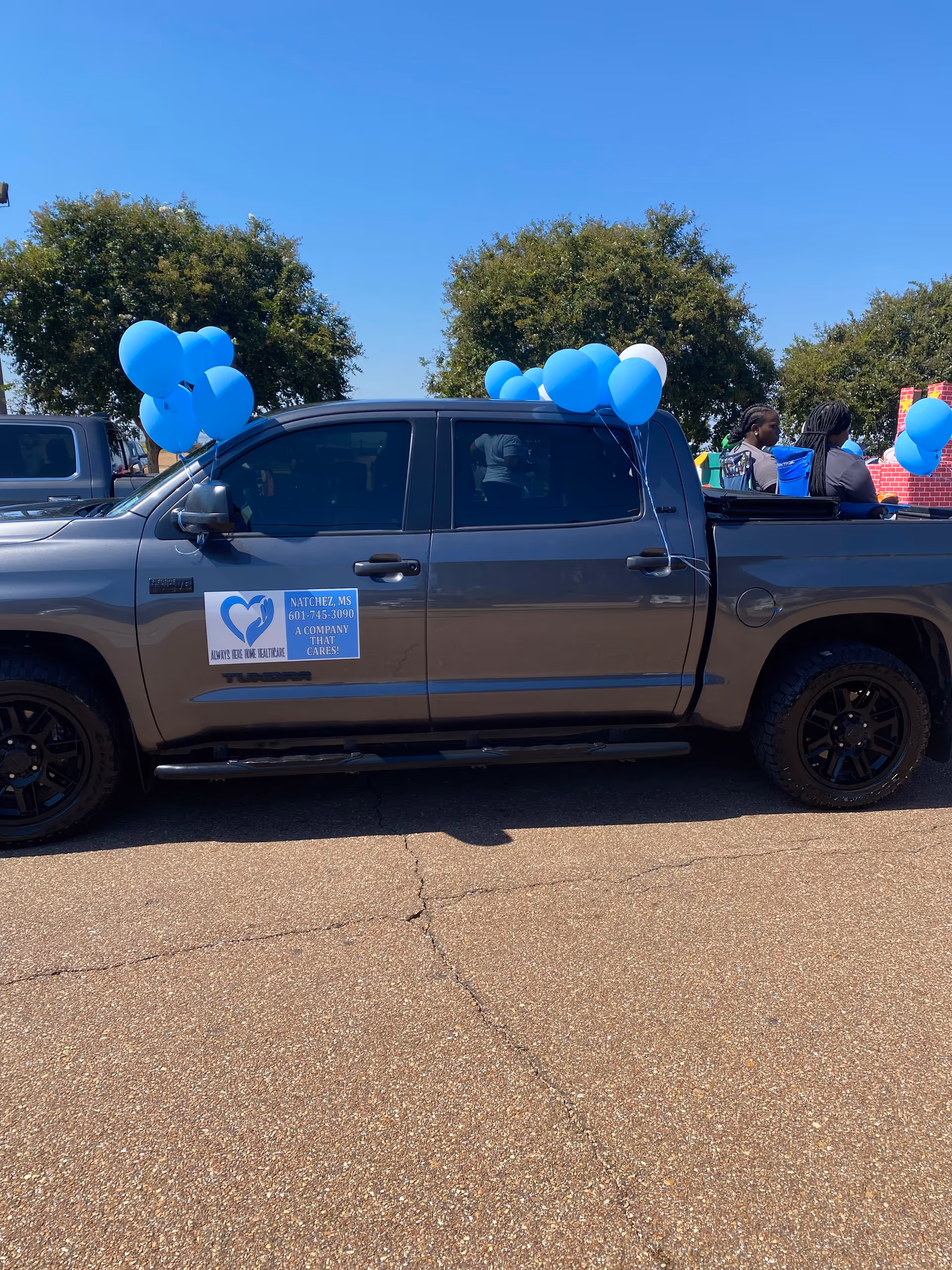 A gray pickup truck with blue balloons parked outdoors during an event.